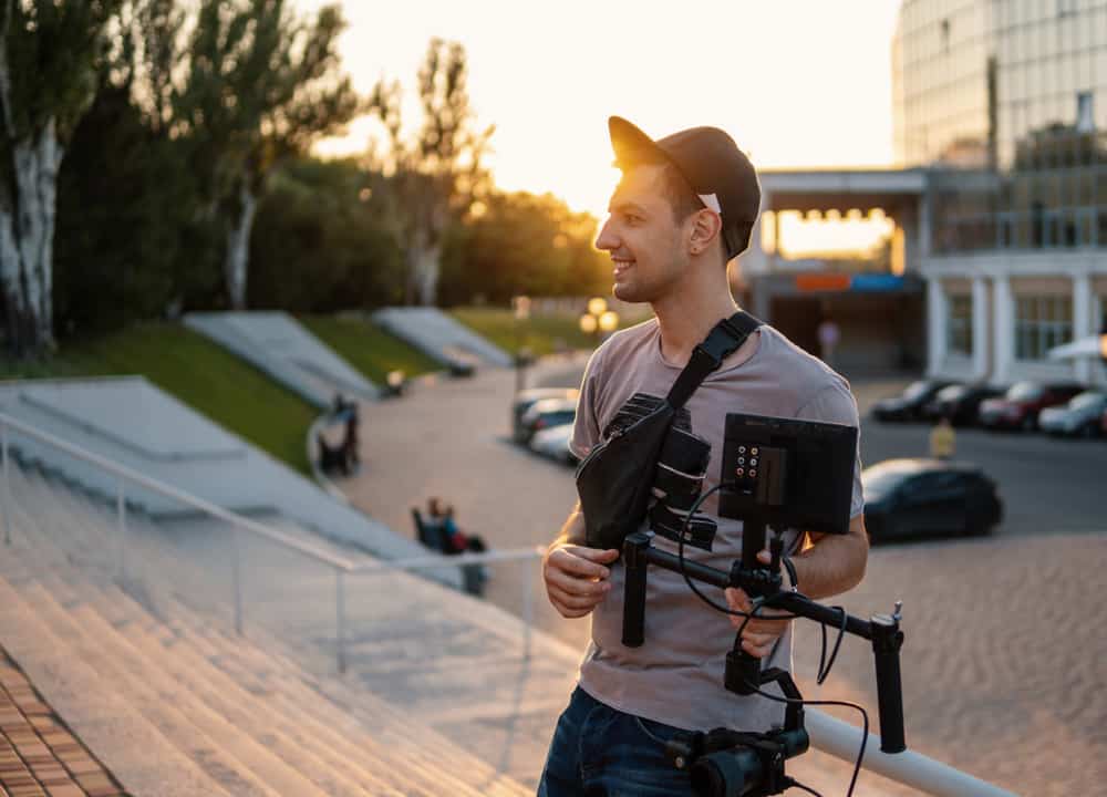 Young male filmmaker shooting short films outdoors with his camera gear