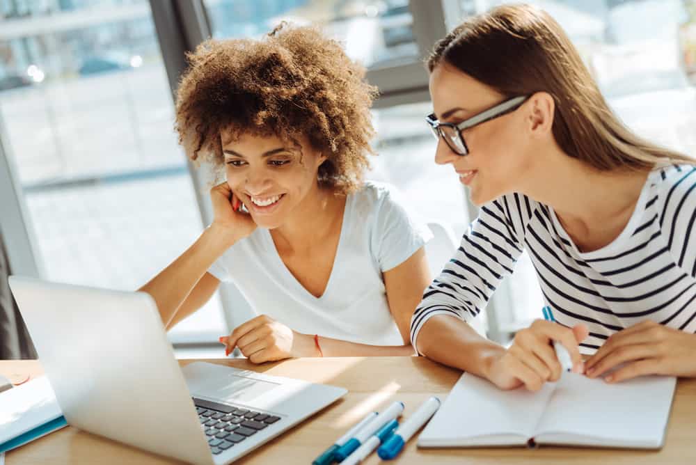 Two female students of an online film school watching a class on a laptop