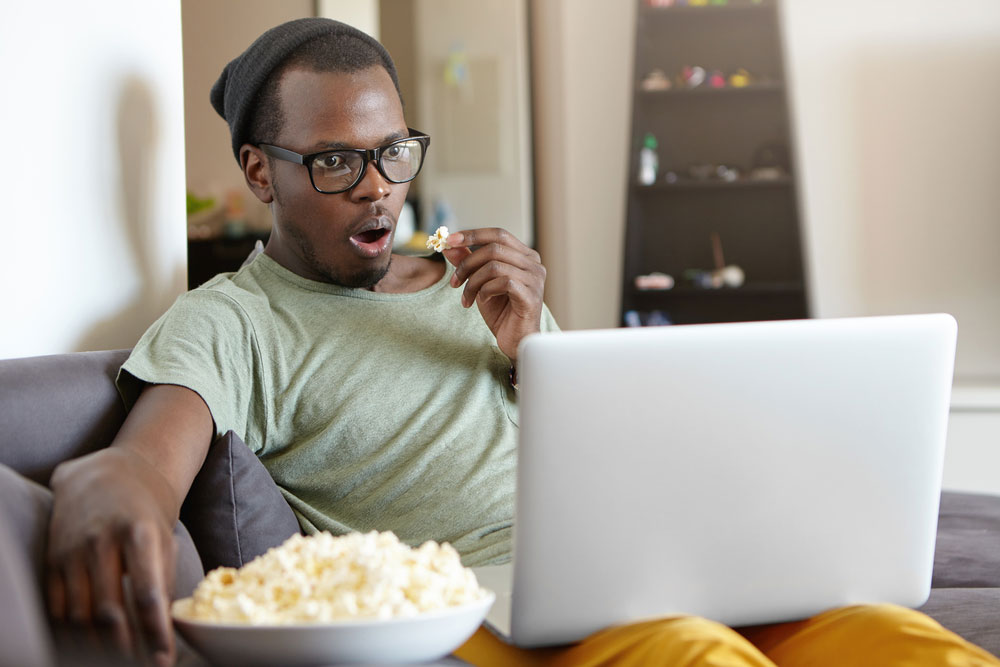 Young black man watching and reviewing a movie while eating popcorn
